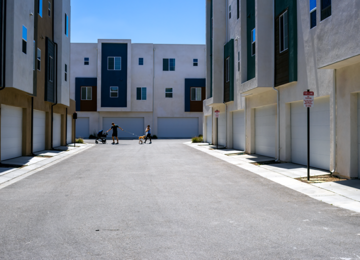 A quiet urban alley framed by sleek modern residential buildings under a summer sky.