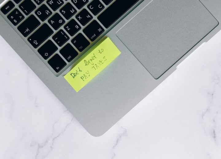 Close-up of a sticky note on a laptop reminding to pay taxes, emphasizing tax season.