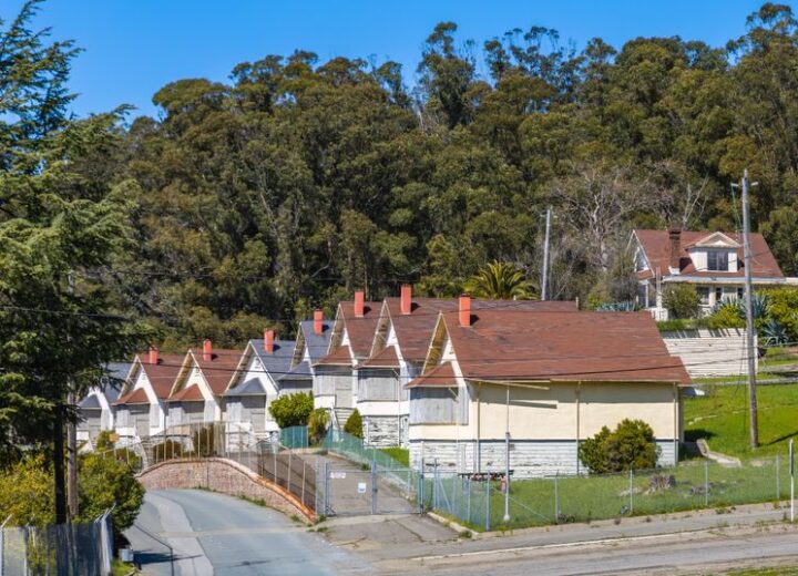 Row of vintage houses beside a serene forest backdrop on a sunny day.