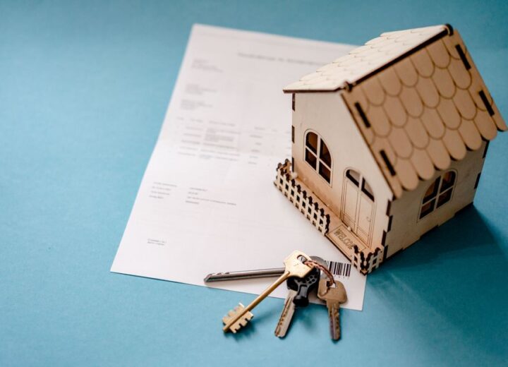Miniature wooden house with keys and contract symbolizing real estate transactions.