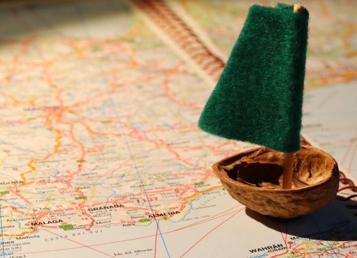 Creative travel metaphor with a tiny sailboat on a detailed world map.