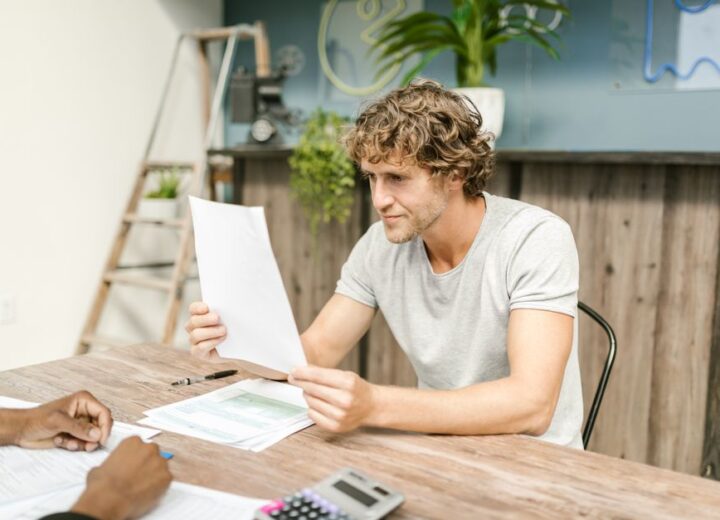 A man with curly hair evaluates documents at a desk, highlighting focused work in a professional setting.