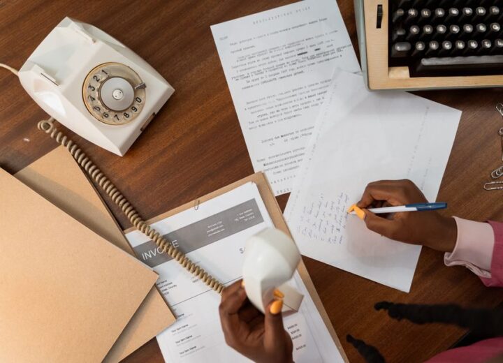 Overhead view of a person writing notes while holding a vintage telephone on a wooden desk.