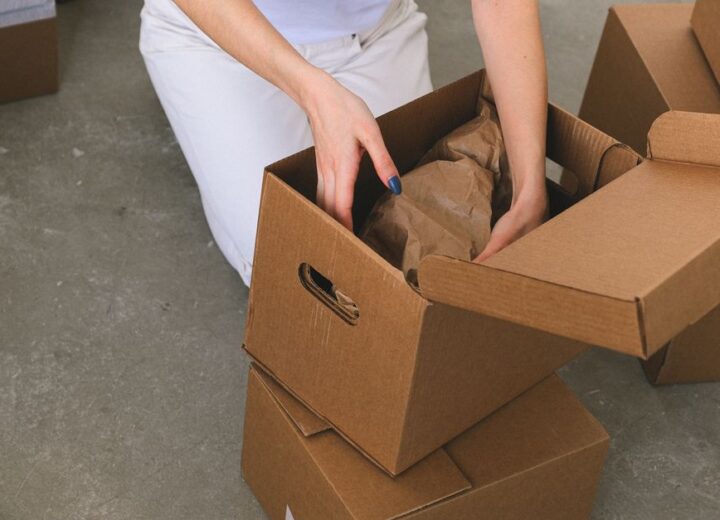 From above of crop anonymous relocating female packing wrapped items into carton box while preparing for moving to new apartment