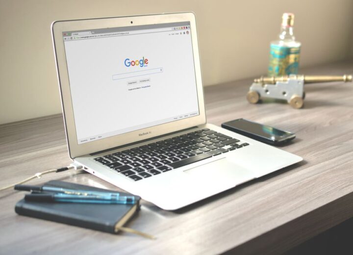 A neat workspace featuring a laptop displaying Google search, a smartphone, and a notebook on a wooden desk.