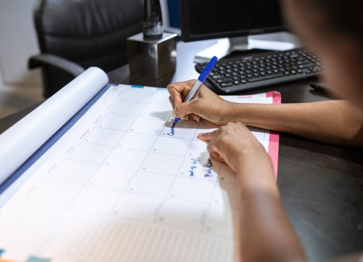 Close-up of a woman planning her schedule on a desk calendar in an office setting.