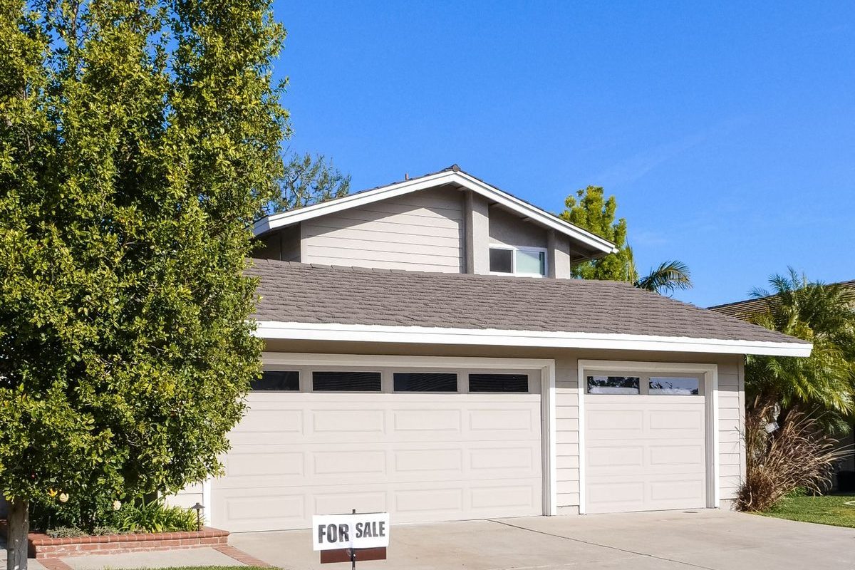 A house with a garage and a for-sale sign in the front yard