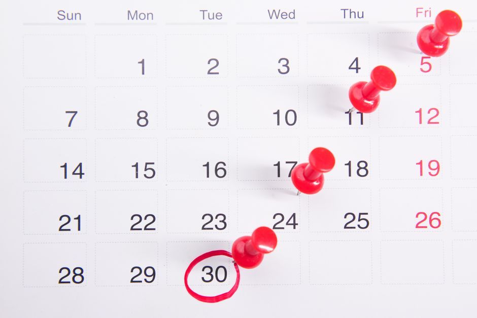 Red pins marking dates on a wall calendar