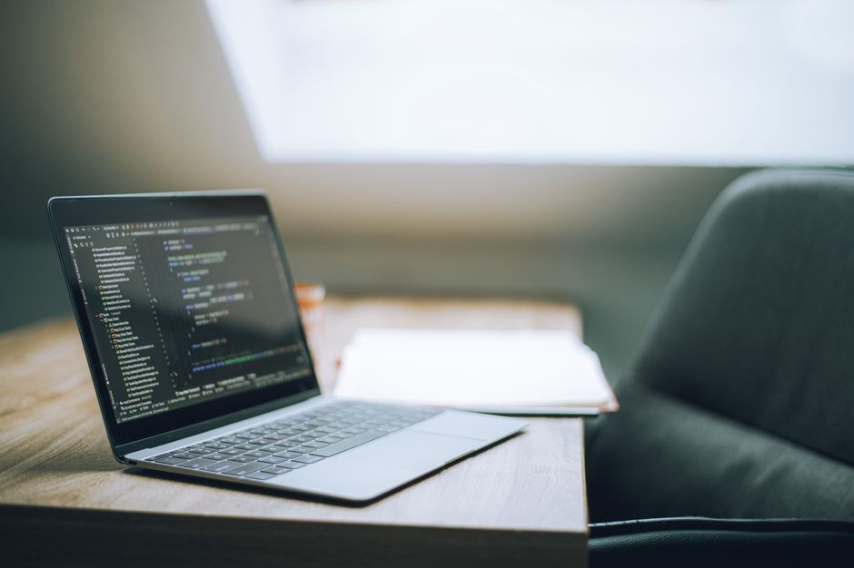 A laptop showing code on a desk by a window