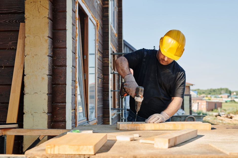 A contractor in a hard hat drilling into a board on a job site