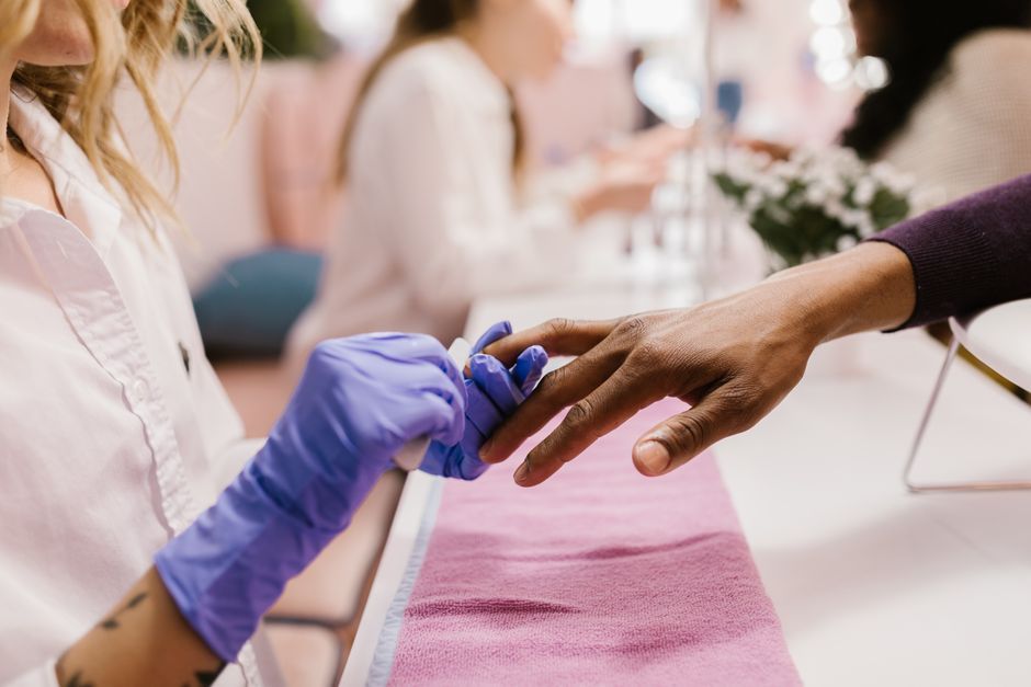 A nail technician in gloves filing a client's nails